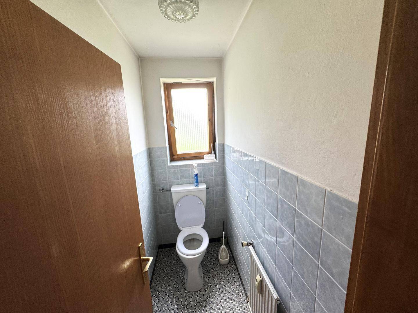 Schmale Gästetoilette mit Fenster, grauen Fliesen und Mosaikboden.