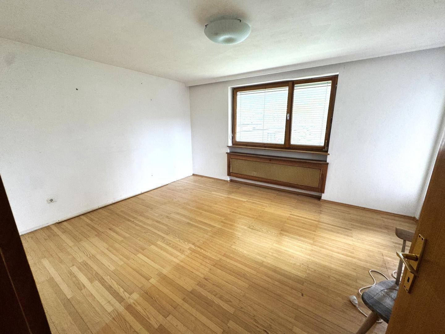 Helles, leeres Zimmer mit Parkettboden und großem Fenster, ideal als Schlafzimmer.