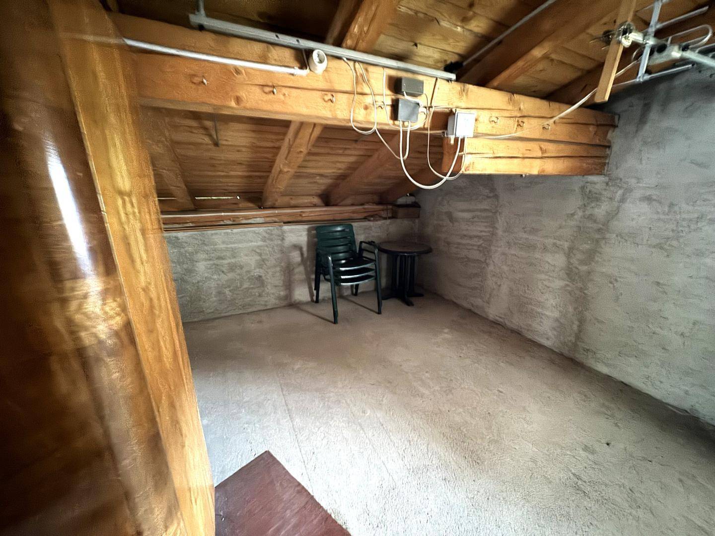 Einfacher Dachbodenraum mit Holzbalken und einem Stuhl, ideal als Abstellfläche.