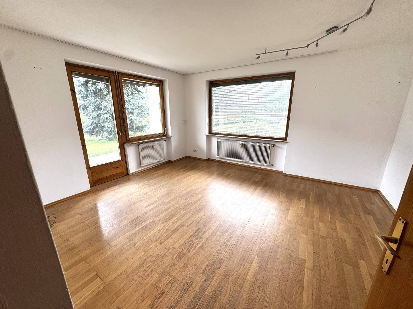 Helles, leeres Zimmer mit Parkettboden und Zugang zum Außenbereich durch eine Fenstertür.