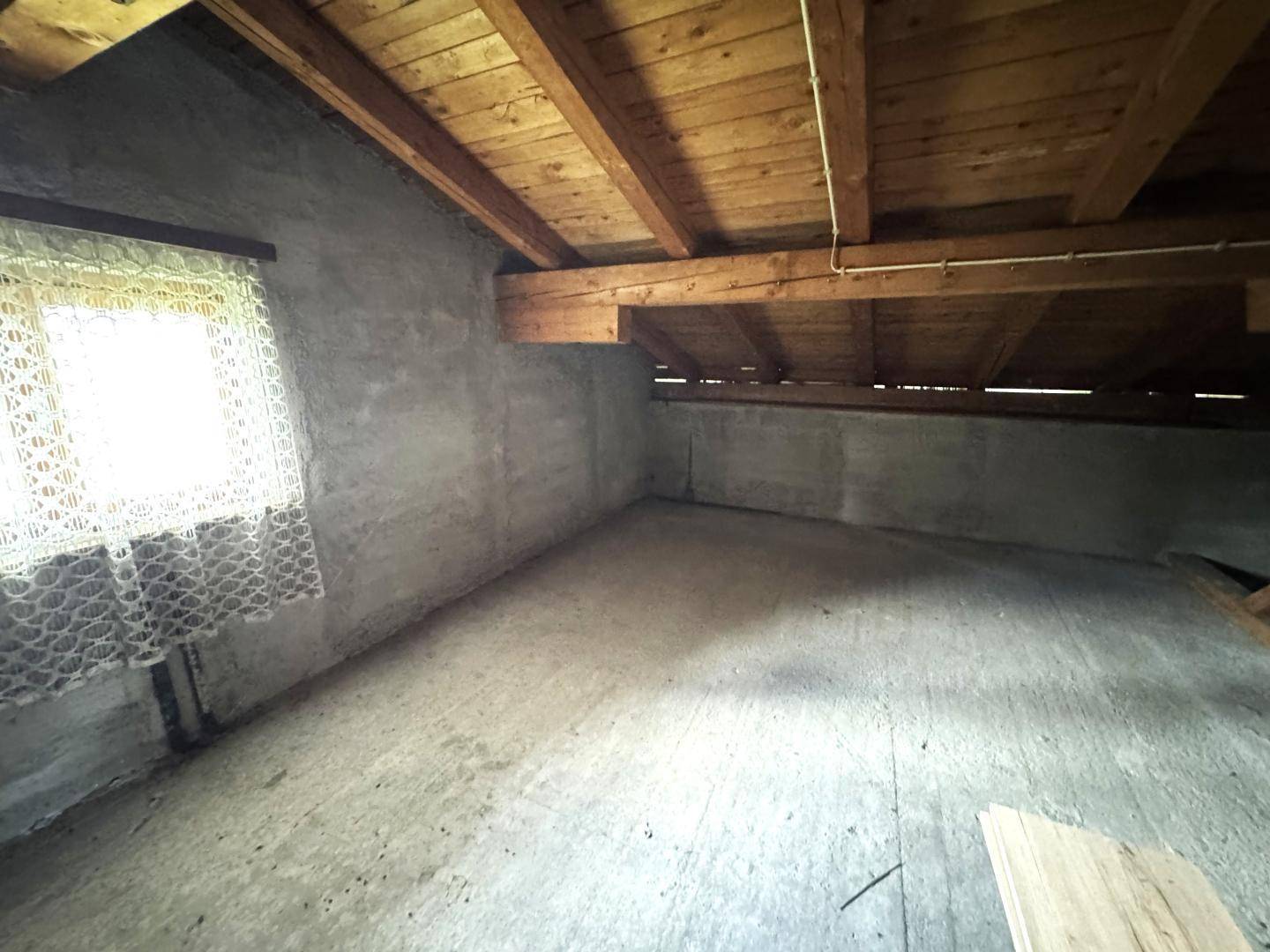 Unausgebauter Dachboden mit sichtbaren Holzbalken und kleinem Fenster.