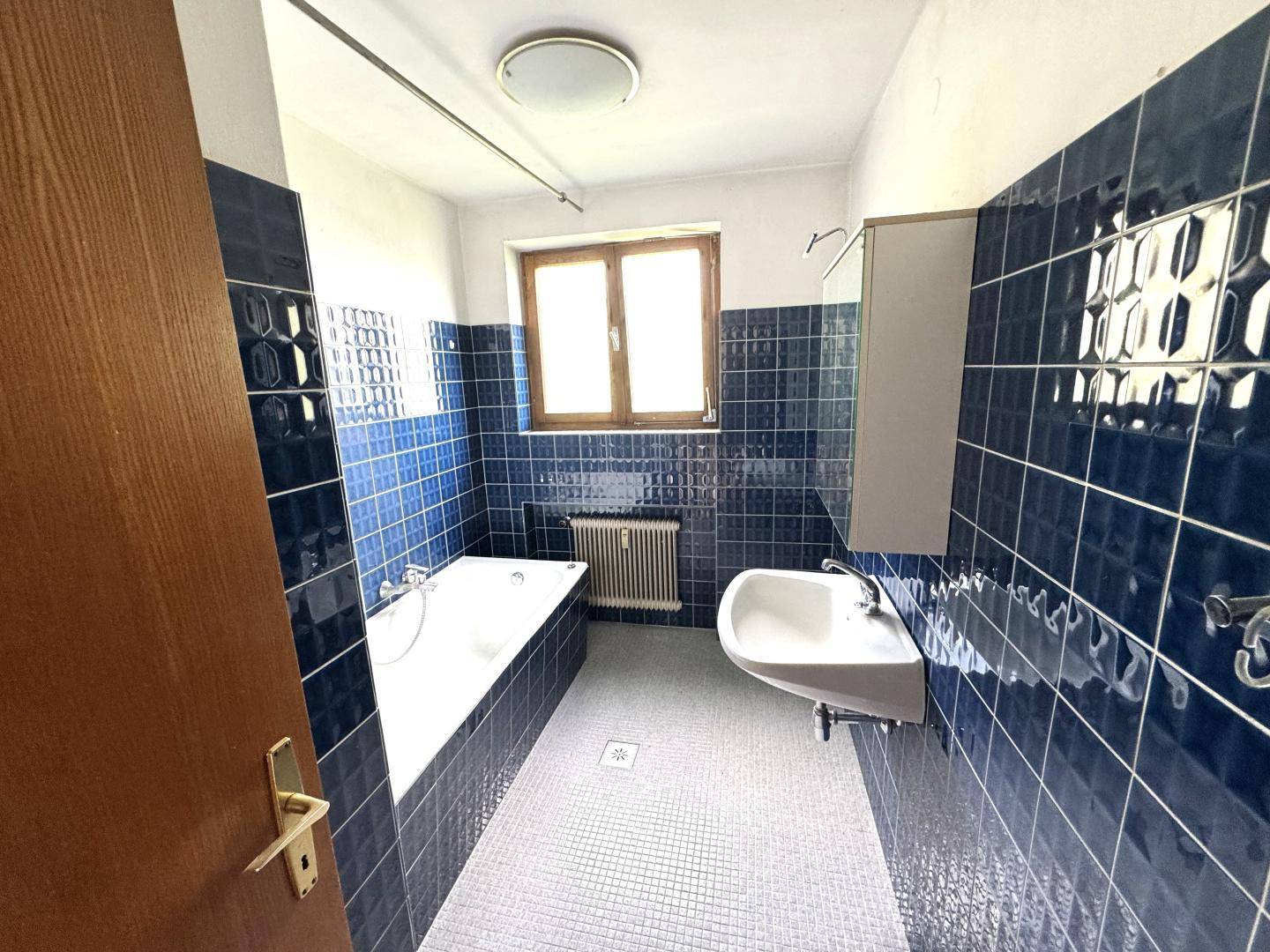 Badezimmer mit Badewanne, Waschbecken und blauen Fliesen im 80er-Jahre-Stil.