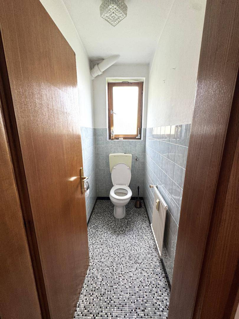 Schmale Gästetoilette mit Fenster, grauen Fliesen und Mosaikboden.