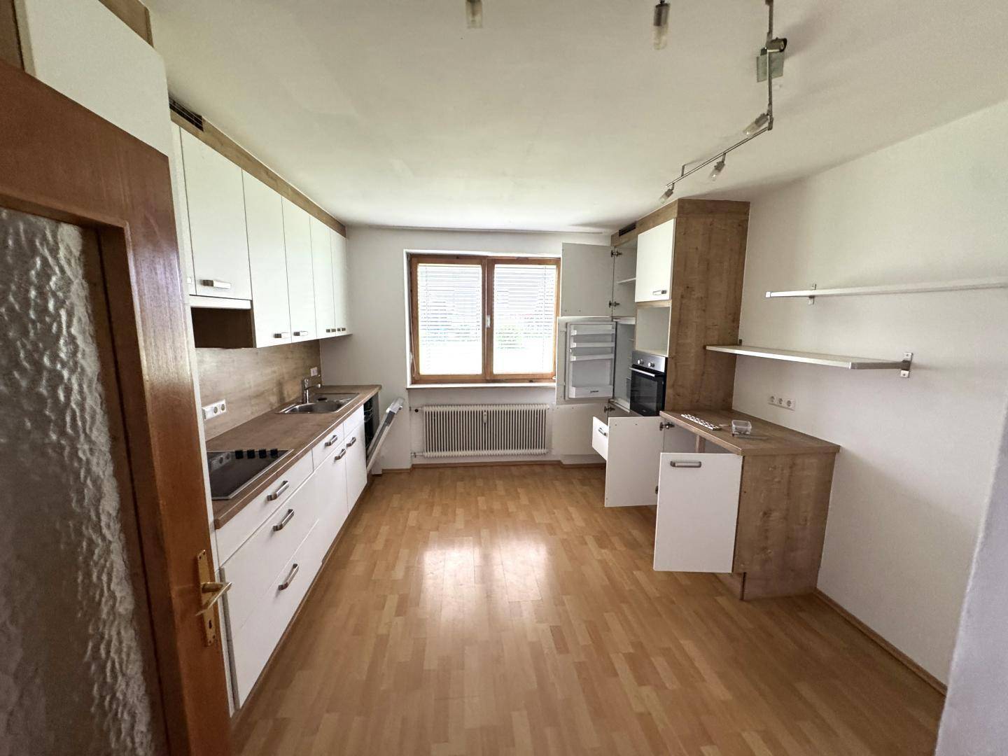 Leere Küche mit weißen Oberschränken, Holzoptik-Unterschränken und Fenster.