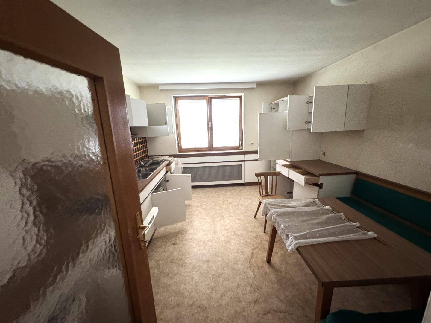 Küche mit weißen Schränken, Essbereich und Fenster, bereit zur Modernisierung.