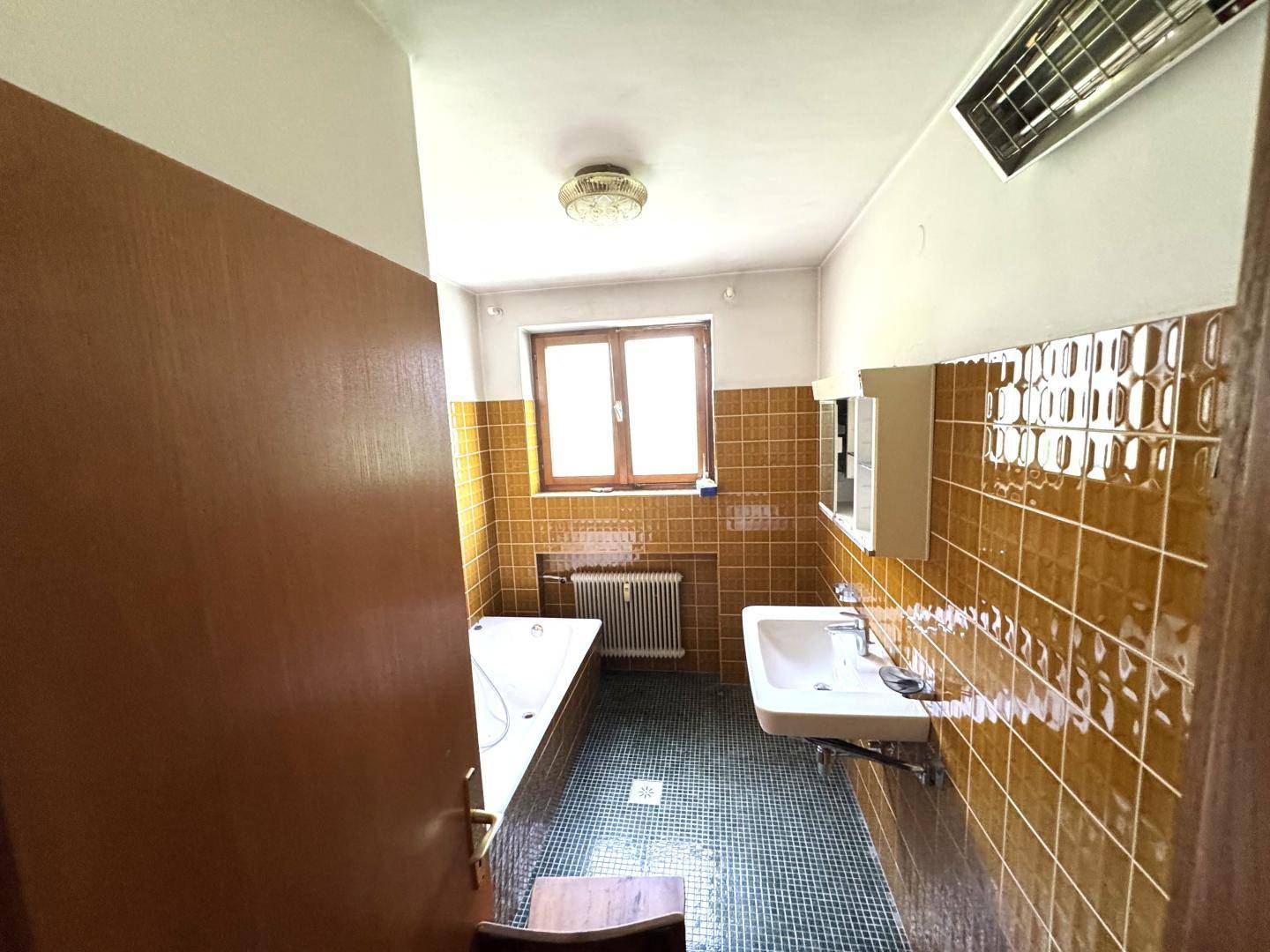 Badezimmer mit Badewanne, Waschbecken und gelb-braunen Fliesen im Retro-Stil.