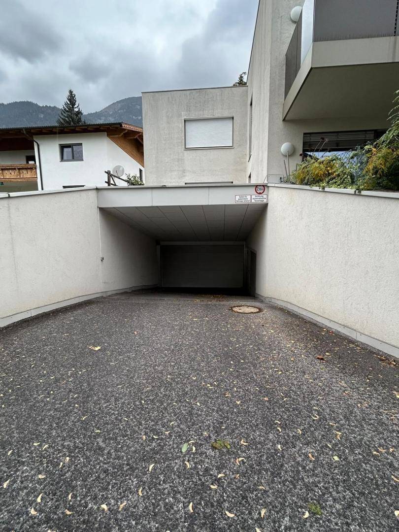 Einfahrt zu einer Tiefgarage unter einem modernen Wohngebäude mit umliegender Vegetation und klarem Himmel.