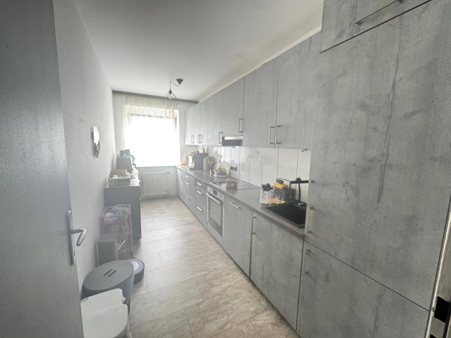 Moderne Küche mit grauen Fronten, Fliesenboden und Fenster für Tageslicht, funktional und hell.