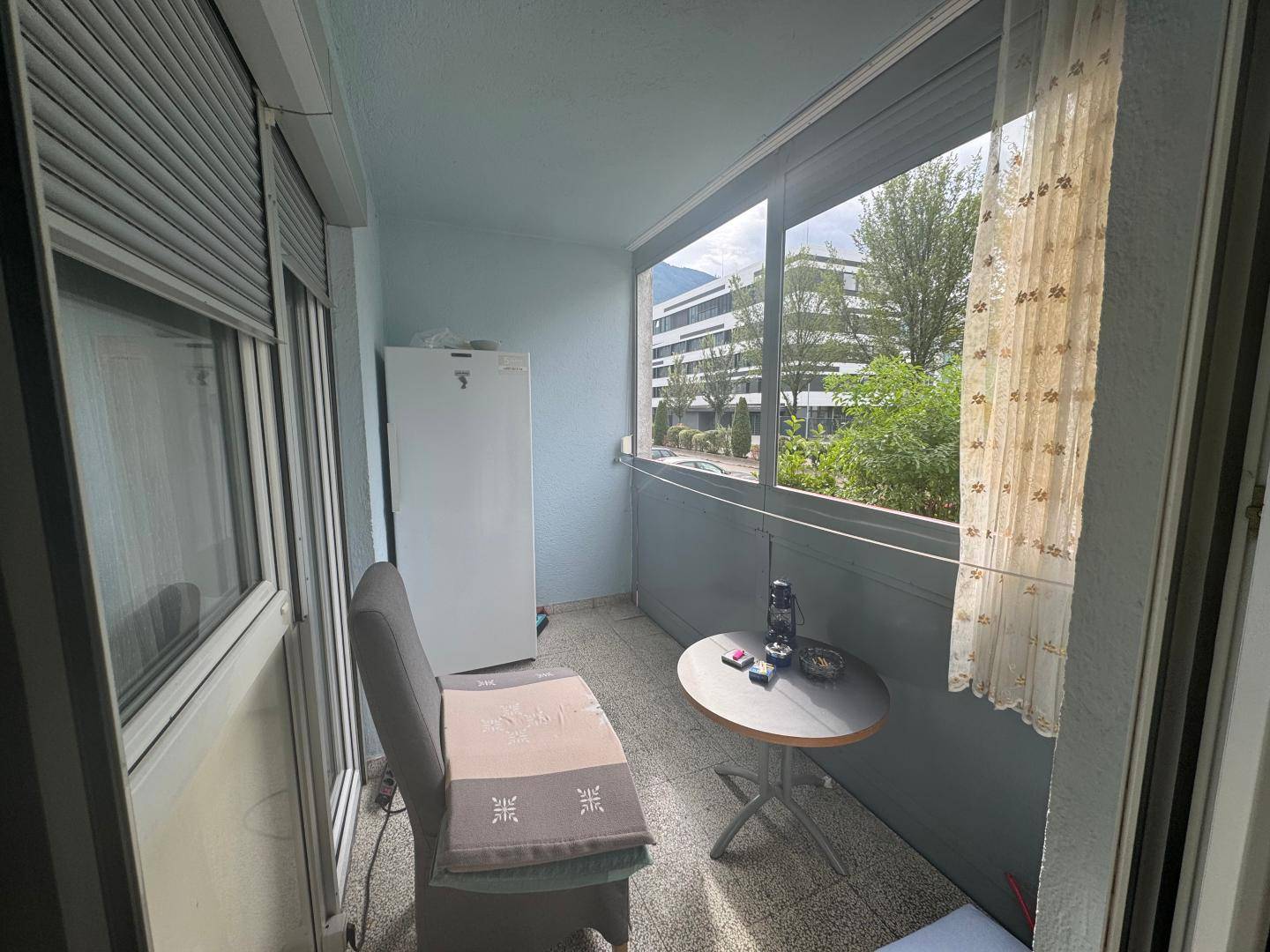 Verglaster Balkon mit Sitzgelegenheit, Kühlschrank und Blick ins Grüne, perfekt zum Entspannen.