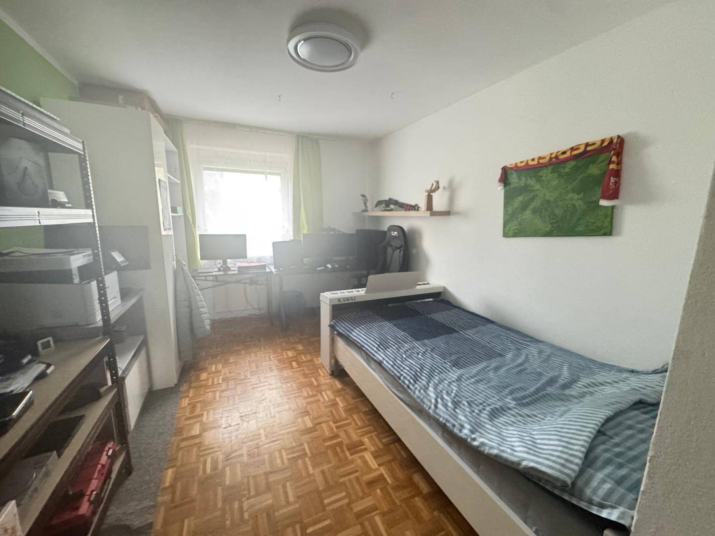 Helles Zimmer mit Einzelbett, Schreibtisch und Regalen für Stauraum, vielseitig nutzbar.