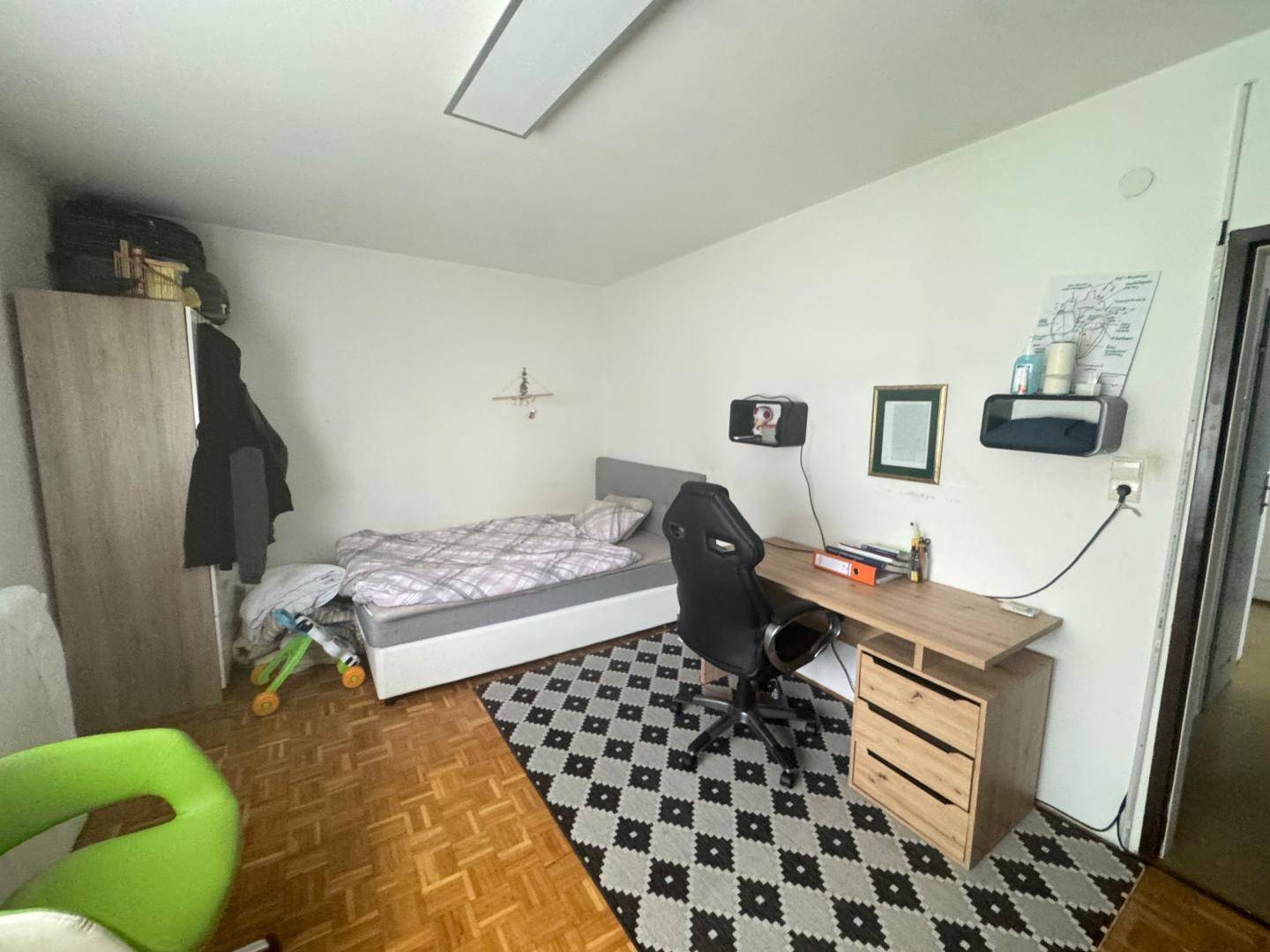 Jugendzimmer mit Einzelbett, Schreibtisch und Teppich auf Parkettboden, ideal zum Lernen und Schlafen.