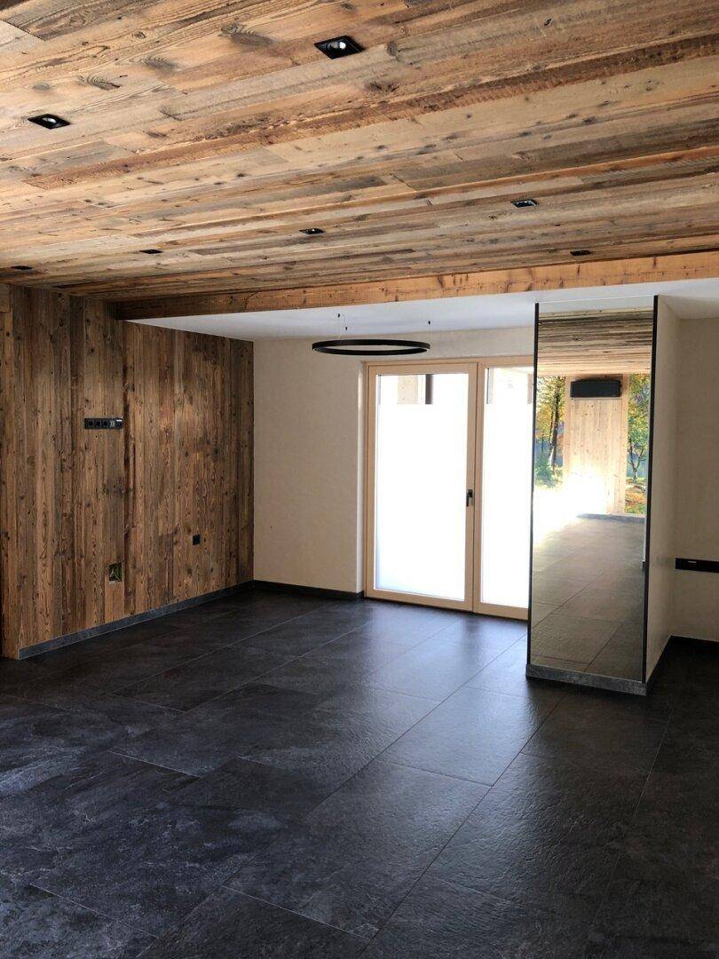Heller Raum mit Holzwandverkleidung, dunklem Fliesenboden und einer großen Spiegelfläche, die den Raum erweitert.