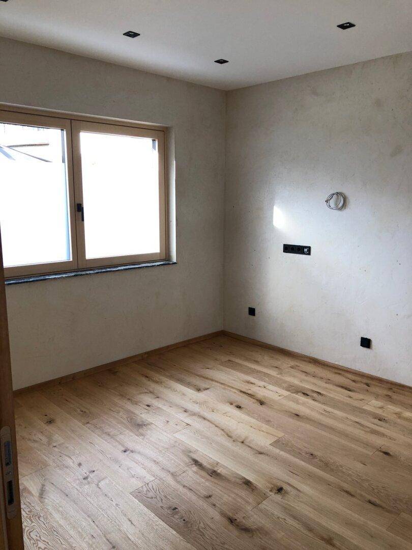 Helles Schlafzimmer mit hellem Holzdielenboden, weißen Wänden und einem großen Fenster für viel Tageslicht.