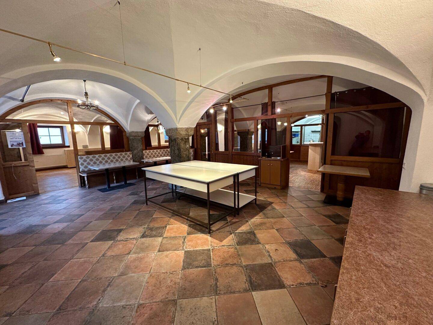 Großer Raum mit Terrakotta-Fliesenboden, Gewölbedecken und rustikalen Holztischen, bereit für Veranstaltungen.