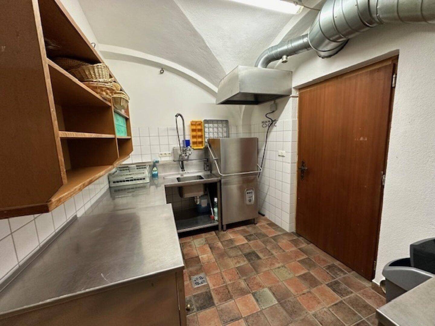 Funktionale Gewerbeküche mit Edelstahlflächen, Spülmaschine und Abluftsystem, bereit für den Betrieb.
