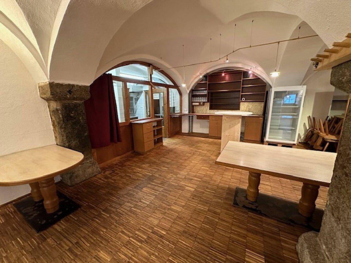 Geräumiger Gewerberaum mit Holzboden, Gewölbedecken und einer Theke, ideal für Gastronomie oder Verkauf.