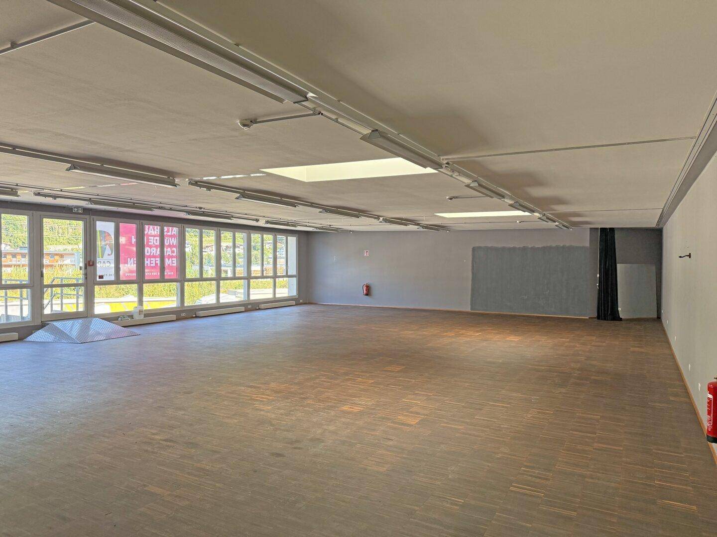 Weitläufiger Gewerberaum mit dunklem Holzfußboden und viel Tageslicht durch die Fenster.