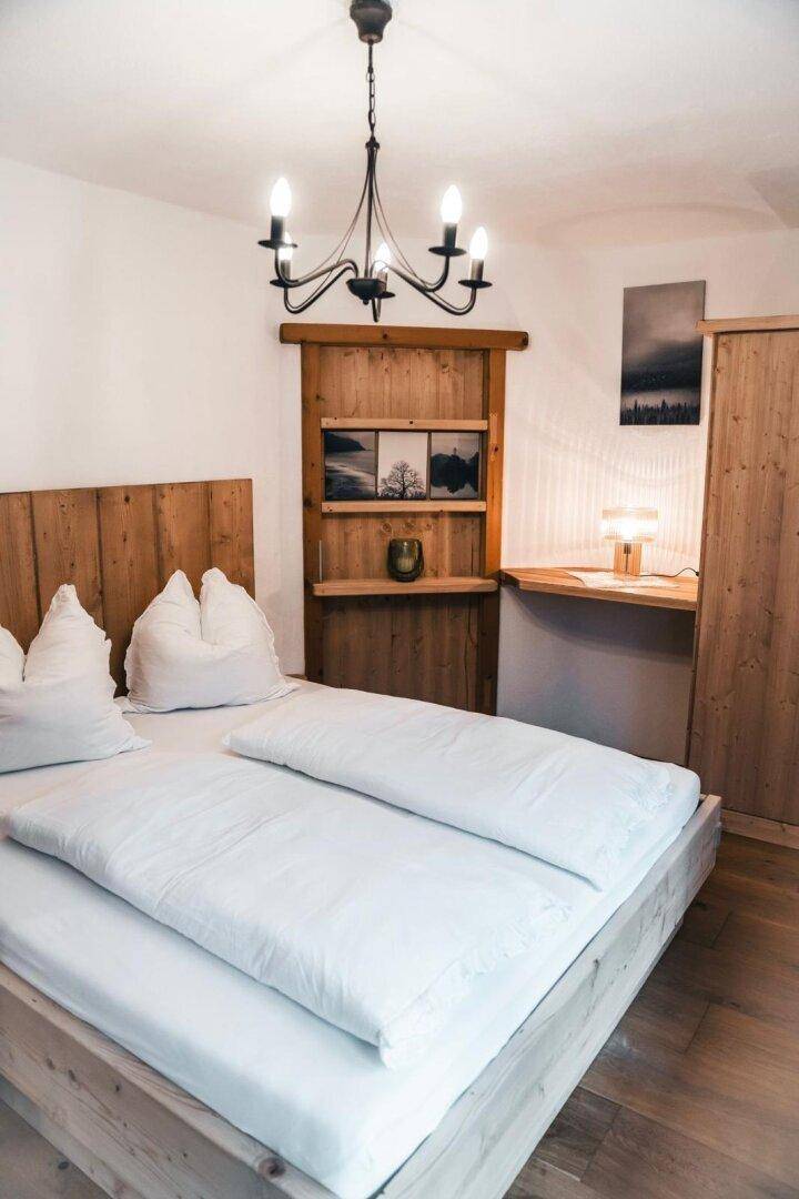 Helles Schlafzimmer mit Holzbett, Holzwandverkleidung und traditionellem Kronleuchter.