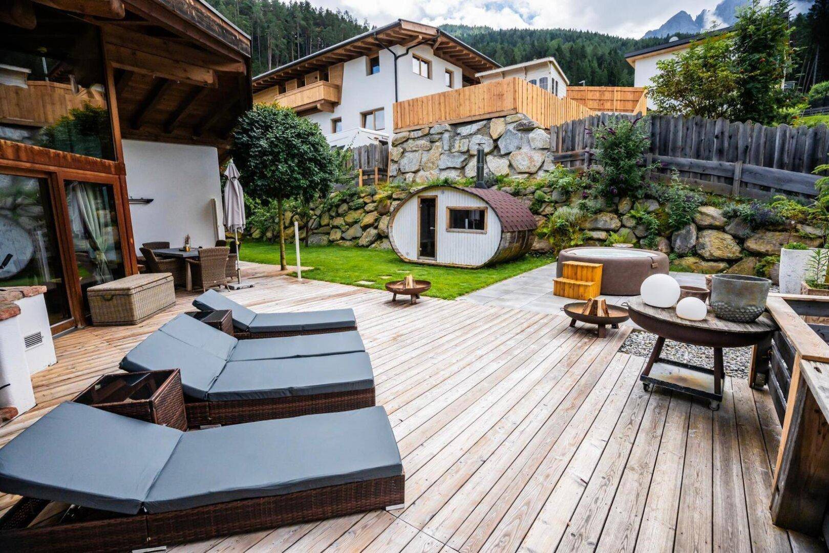 Großzügige Holzterrasse mit Liegestühlen, Fasssauna und Whirlpool im Garten.