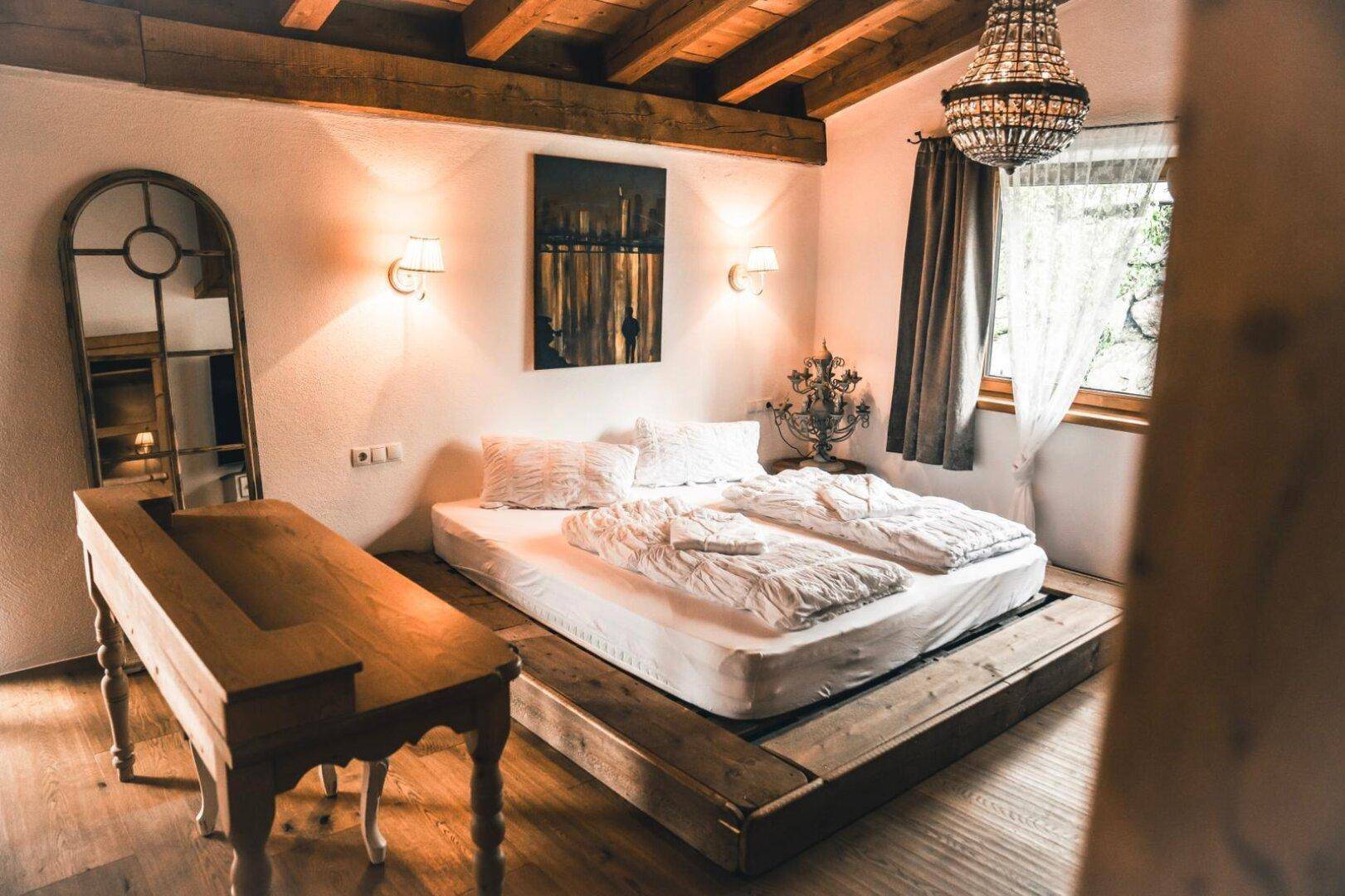Schlafzimmer mit Holzbalkendecke, Doppelbett und rustikalem Kronleuchter.