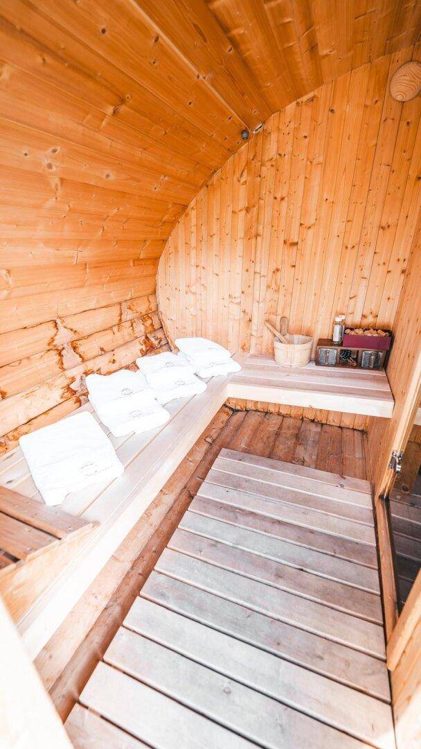 Innenansicht der Holzfasssauna mit Sitzbänken und Saunaofen.