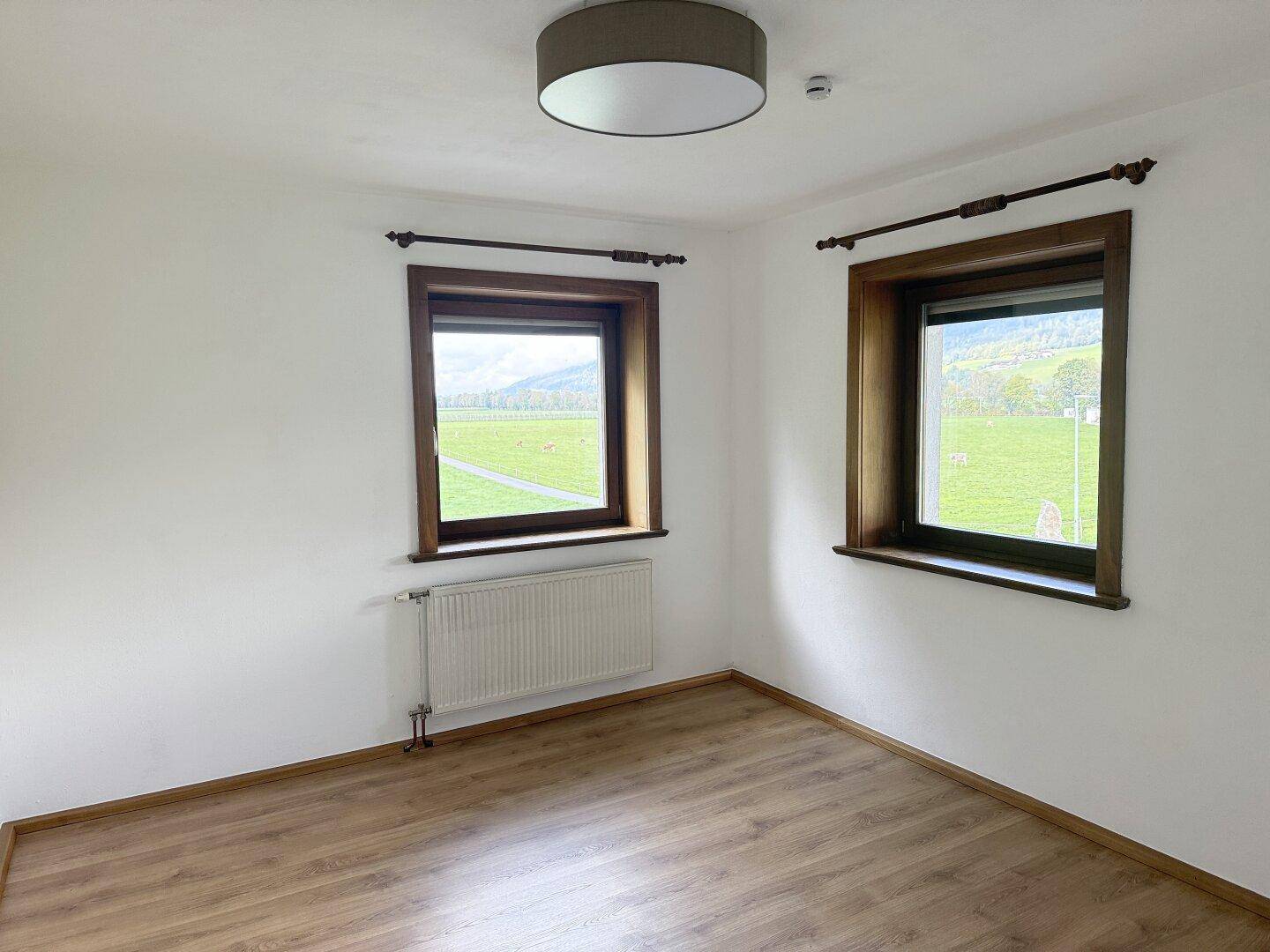 Helles Schlafzimmer mit Laminatboden, weißen Wänden und Blick auf die grüne Landschaft.