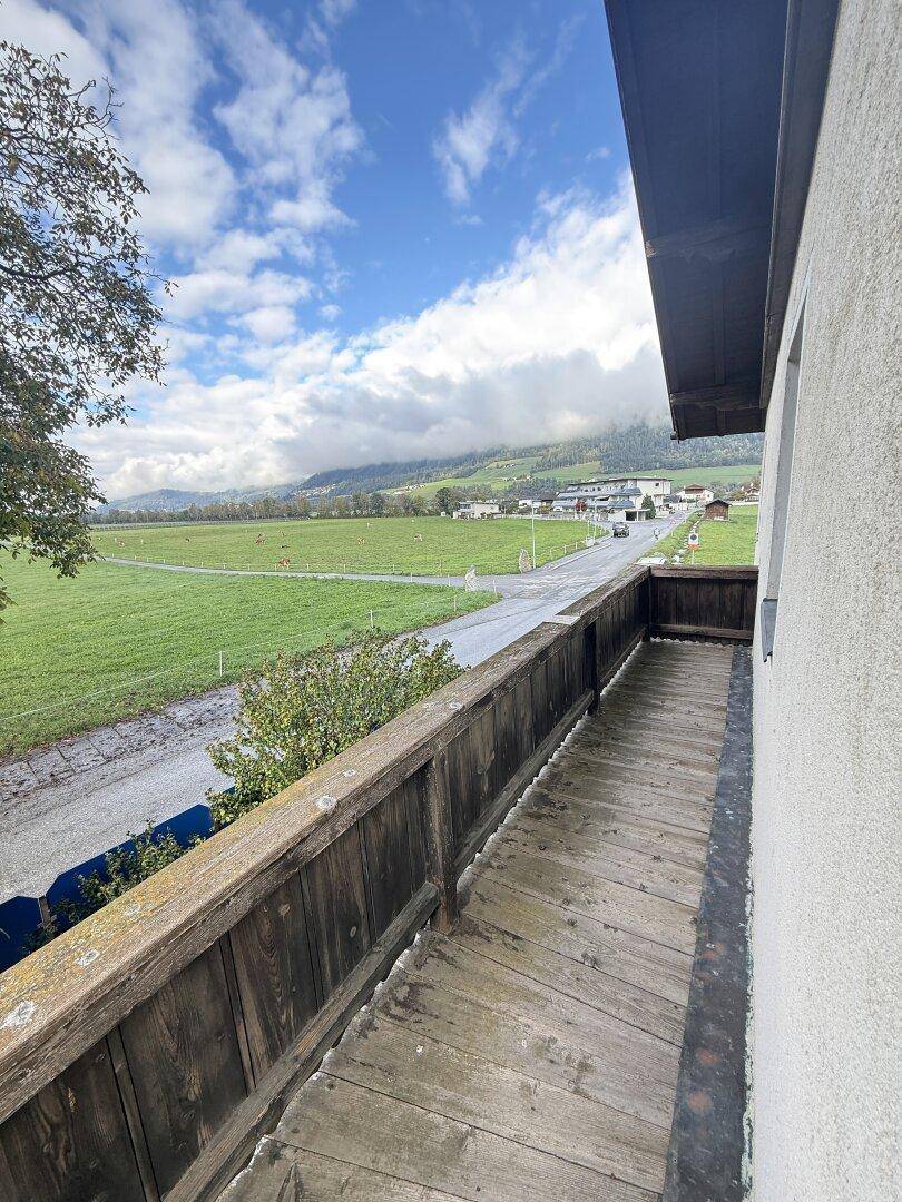 Rustikaler Holzbalkon mit weitem Blick über grüne Felder und die umliegende Berglandschaft.