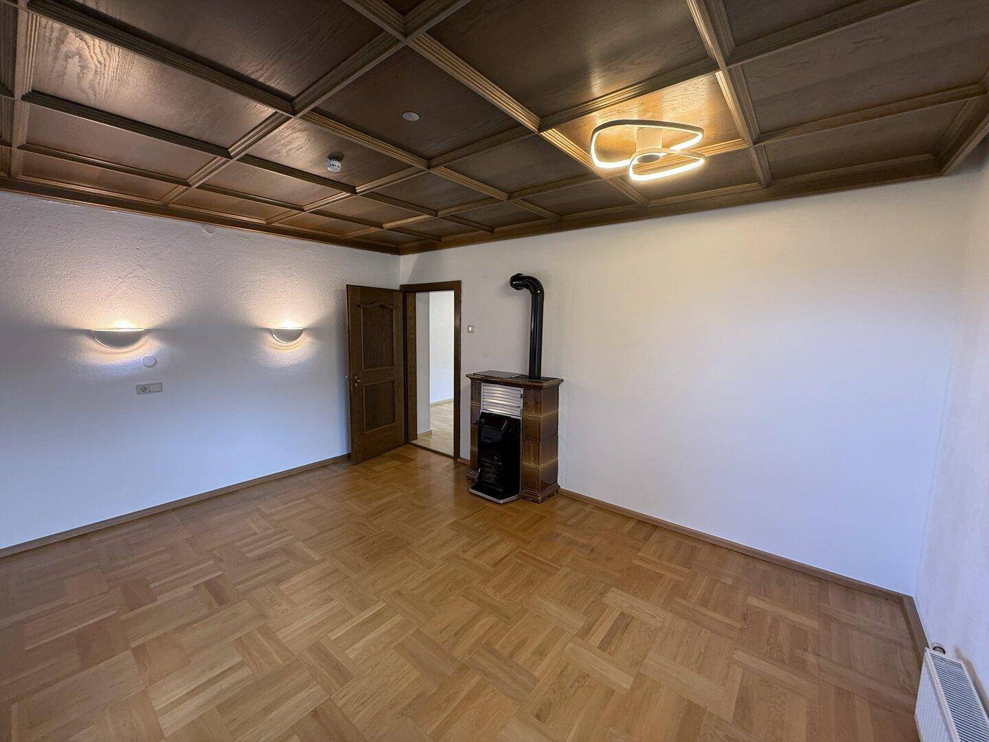 Geräumiges Wohnzimmer mit Fischgrätparkett, Holzkassettendecke und einem Kaminofen.