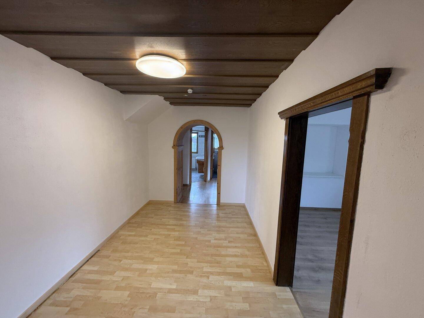 Heller Flur mit Laminatboden und Holzbalkendecke, der zu weiteren Räumen führt.