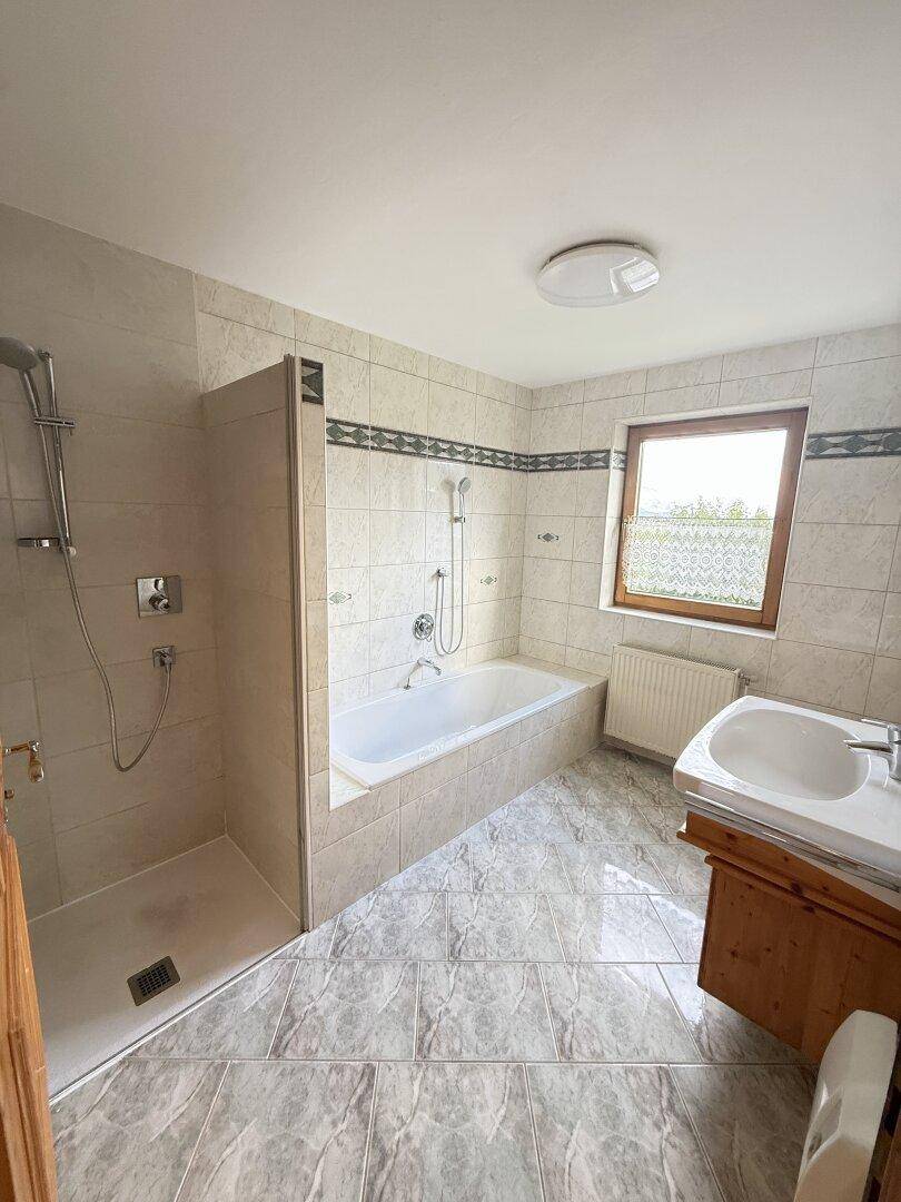 Gefliestes Badezimmer mit Badewanne, Dusche, Einzelwaschbecken und Fenster für Tageslicht.