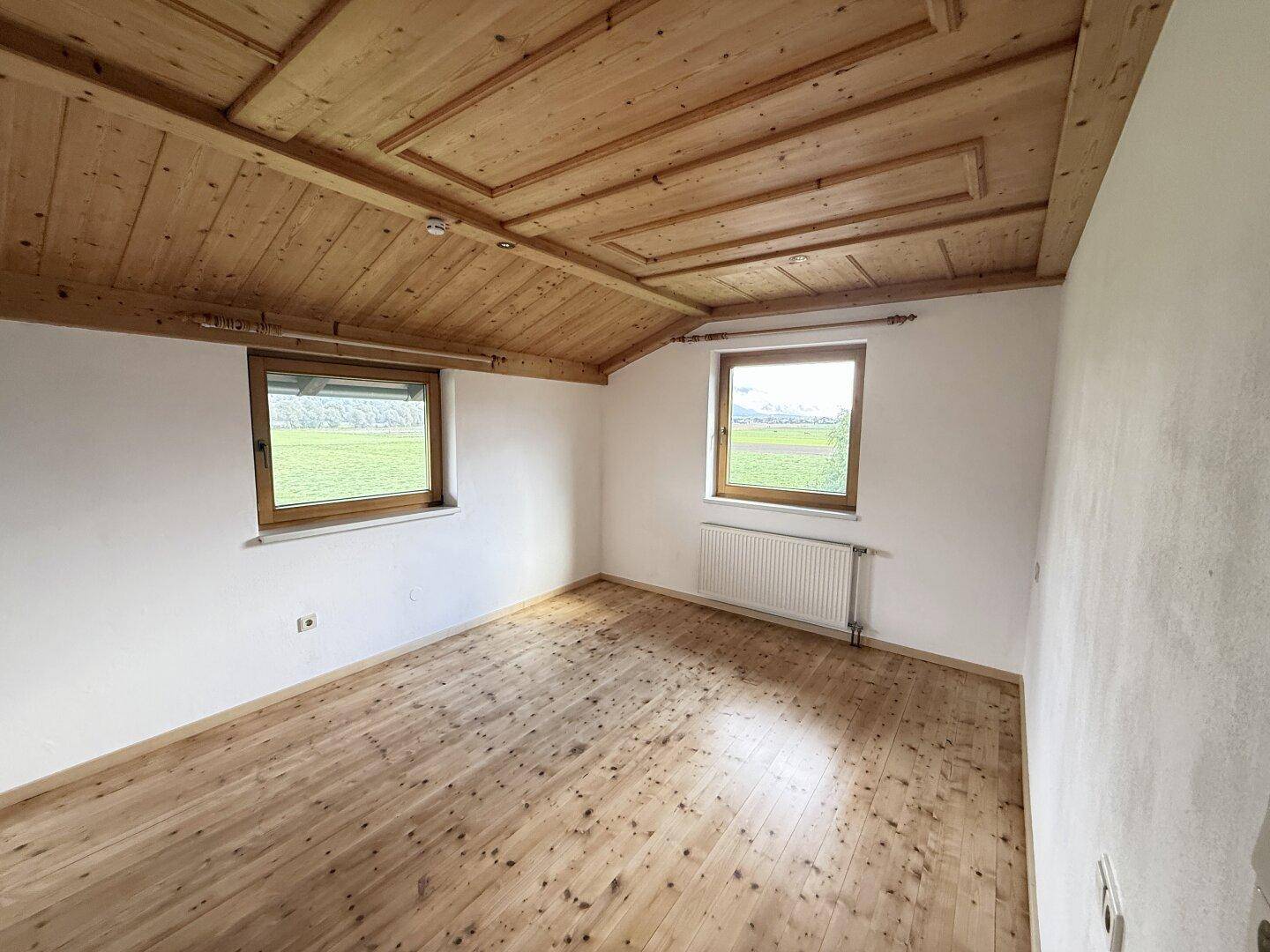 Helles Schlafzimmer mit Holzdielenboden, Holzdecke und Fenstern mit Blick auf die Landschaft.