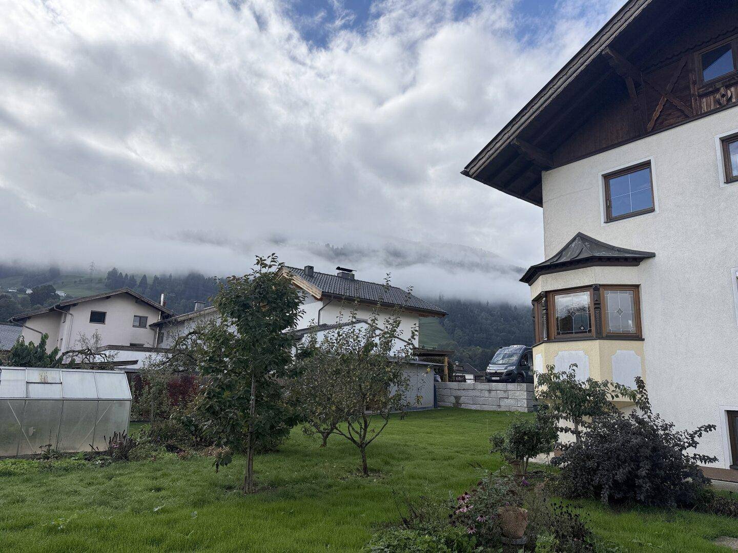 Gartenbereich mit Rasenfläche, Obstbäumen und Blick auf die Häuser der Nachbarschaft und Berge.