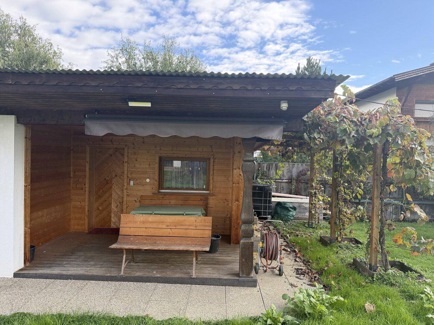 Überdachte Holzterrasse mit Sitzbank und Weinreben, ideal für entspannte Stunden im Freien.