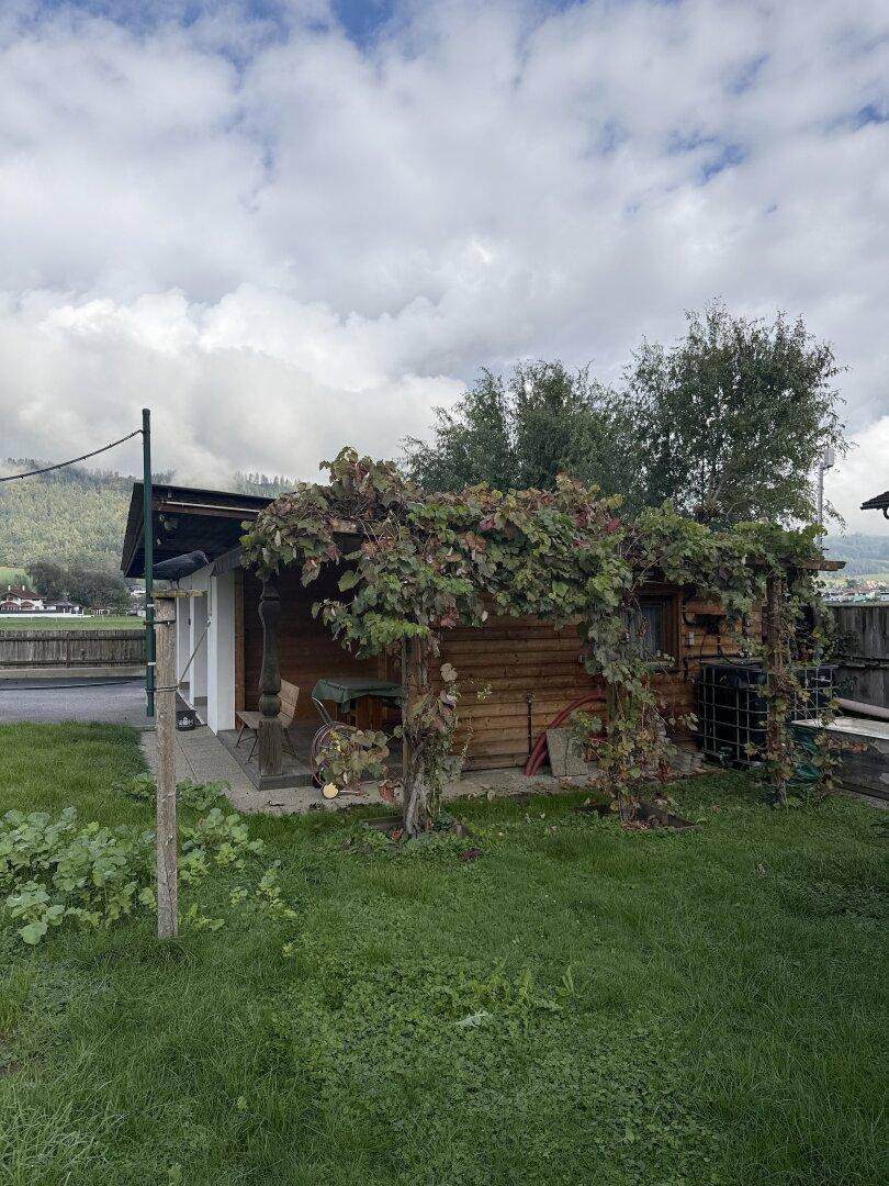 Rustikales Gartenhaus mit überdachtem Sitzbereich und üppigem Bewuchs.