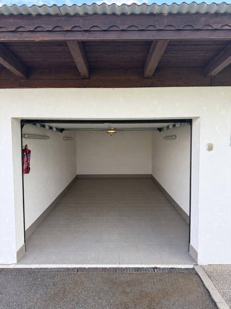 Leere Garage mit gefliestem Boden, weiß gestrichenen Wänden und einem Feuerlöscher.