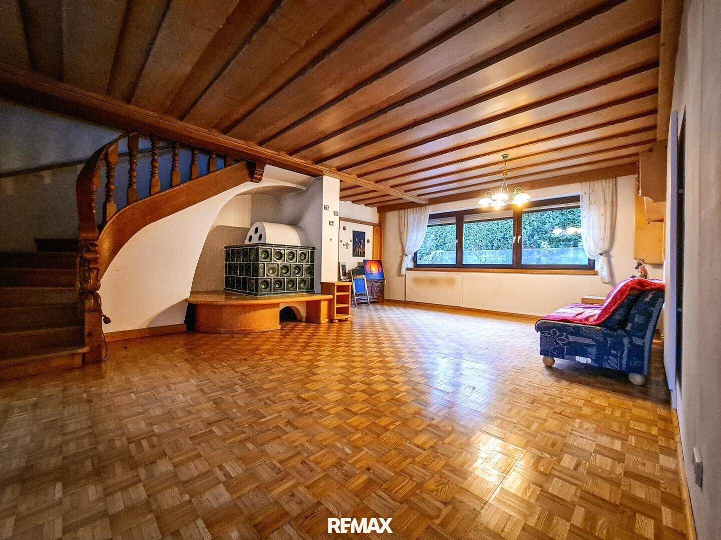 Geräumiges Wohnzimmer mit Kachelofen, Holzbalkendecke und Parkettboden.