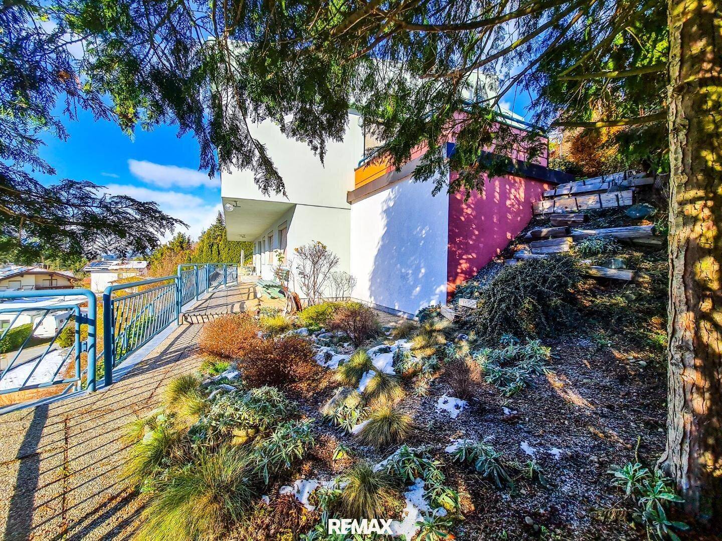 Außenansicht des Gebäudes mit einem Weg entlang der Fassade und winterlicher Bepflanzung.
