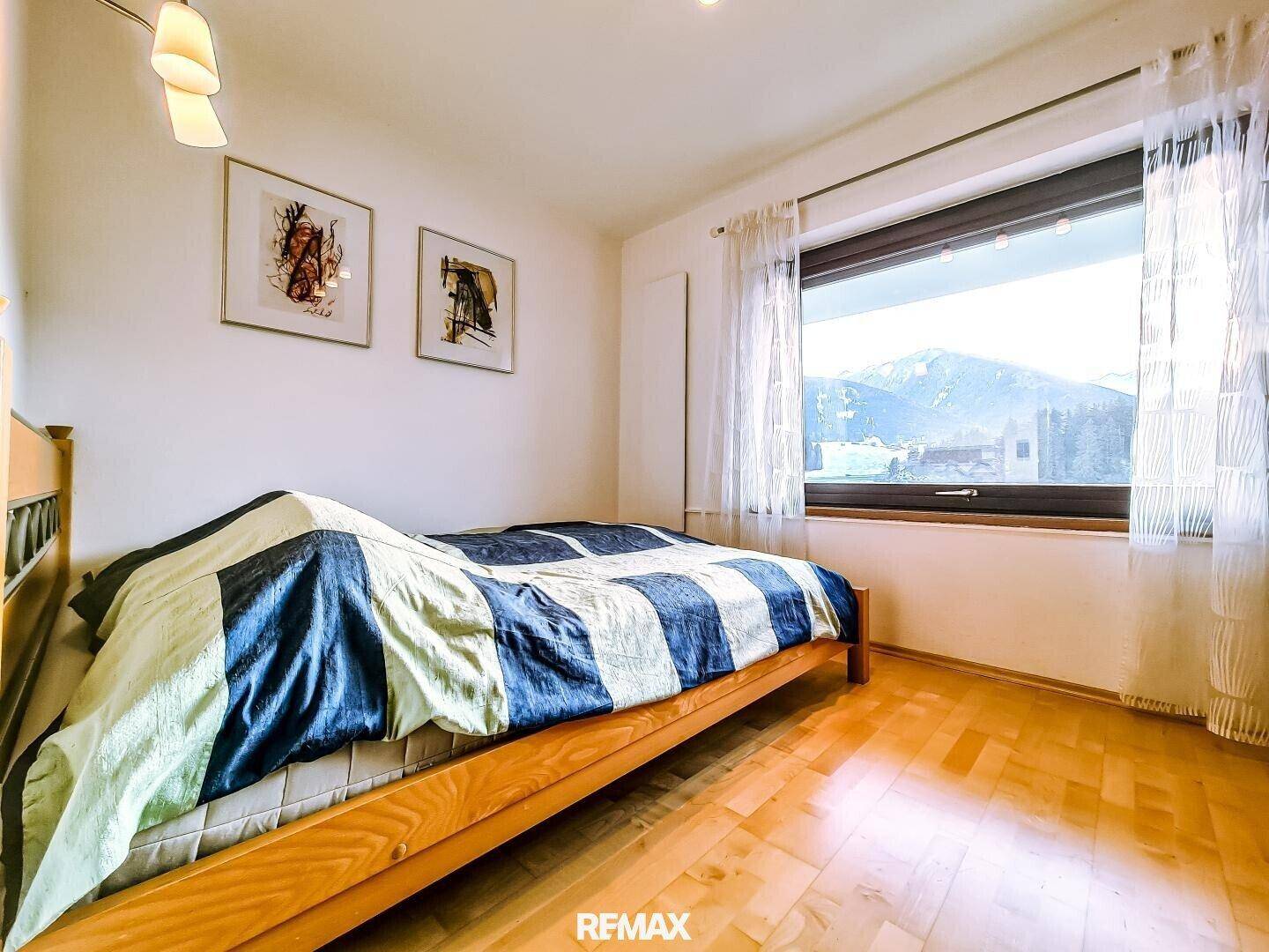 Helles Schlafzimmer mit Doppelbett, Parkettboden und Bergblick durch das große Fenster.
