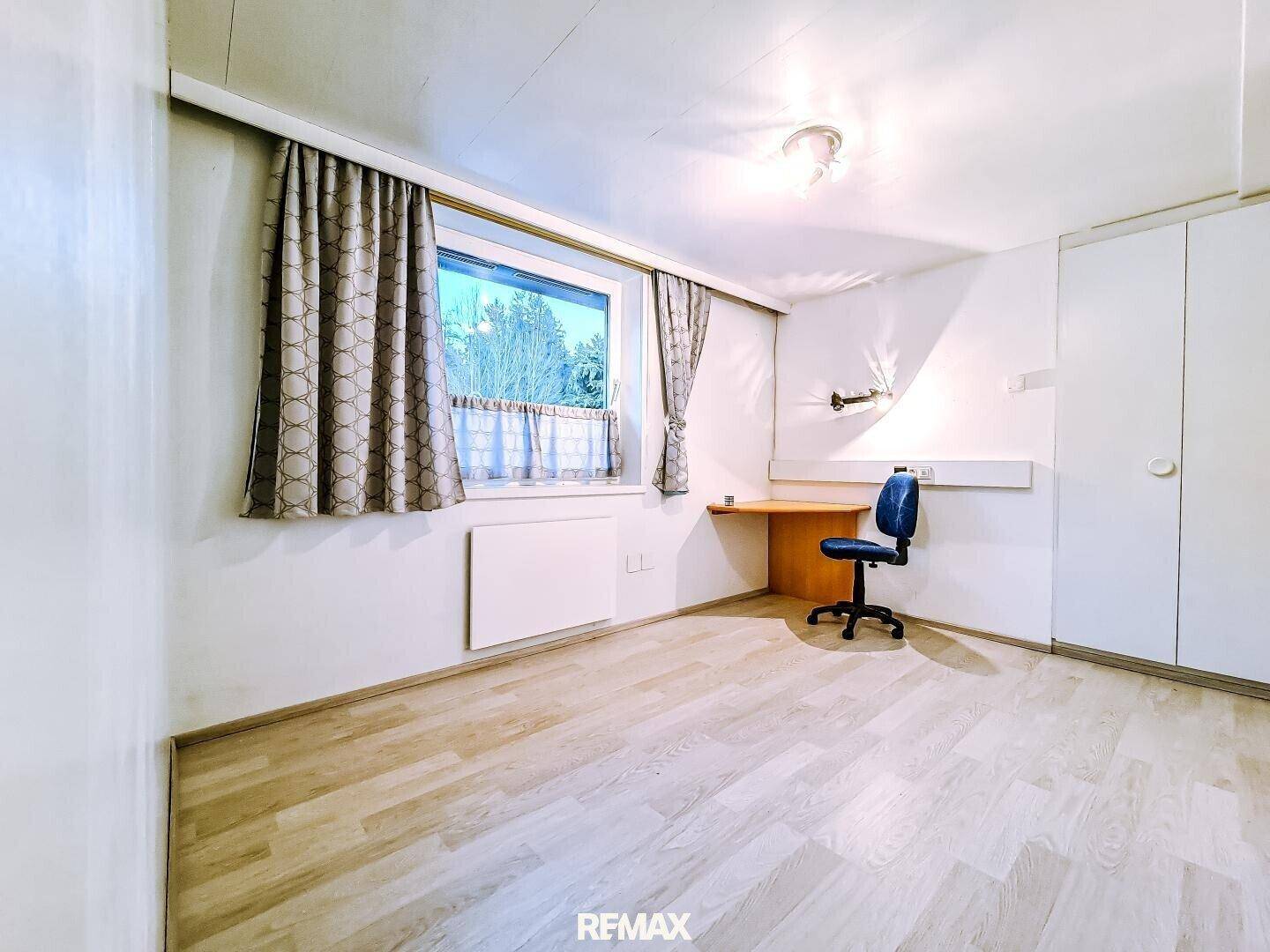Helles Zimmer mit Laminatboden, Fenster und integriertem Schreibtischbereich.