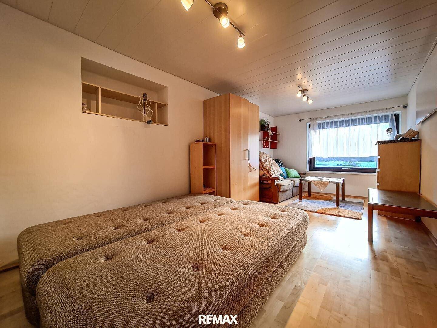 Schlafzimmer mit zwei Einzelbetten, Holzdecke und hellem Parkettboden, funktional eingerichtet.