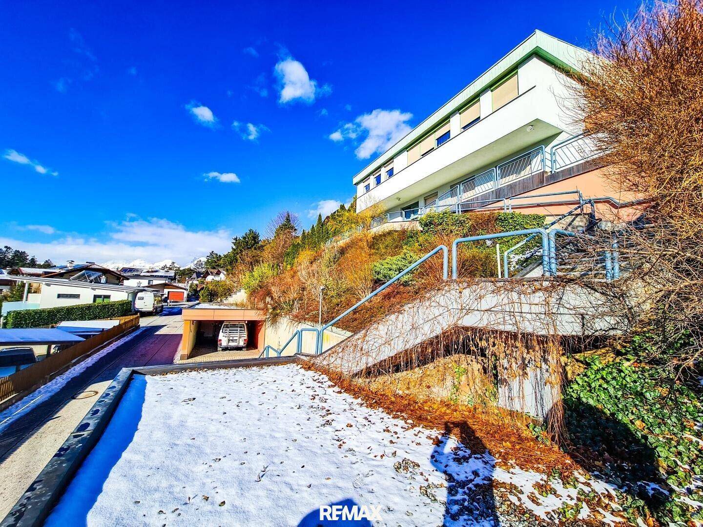 Ansicht des Hauses von unten mit Zufahrt und verschneitem Vorgarten in bergiger Umgebung.