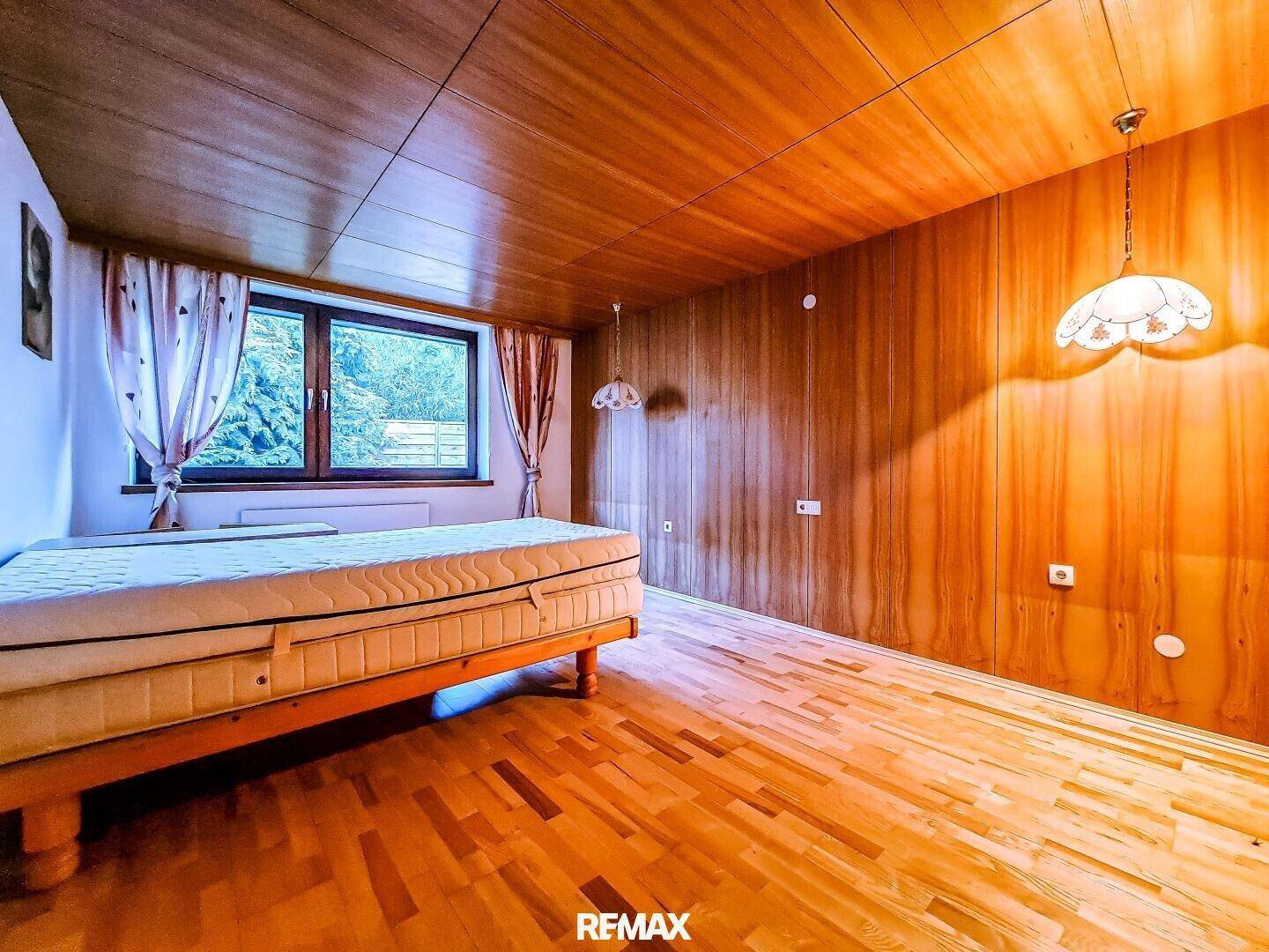 Schlafzimmer mit Holztäfelung, Holzboden und Fenster mit Blick ins Grüne.