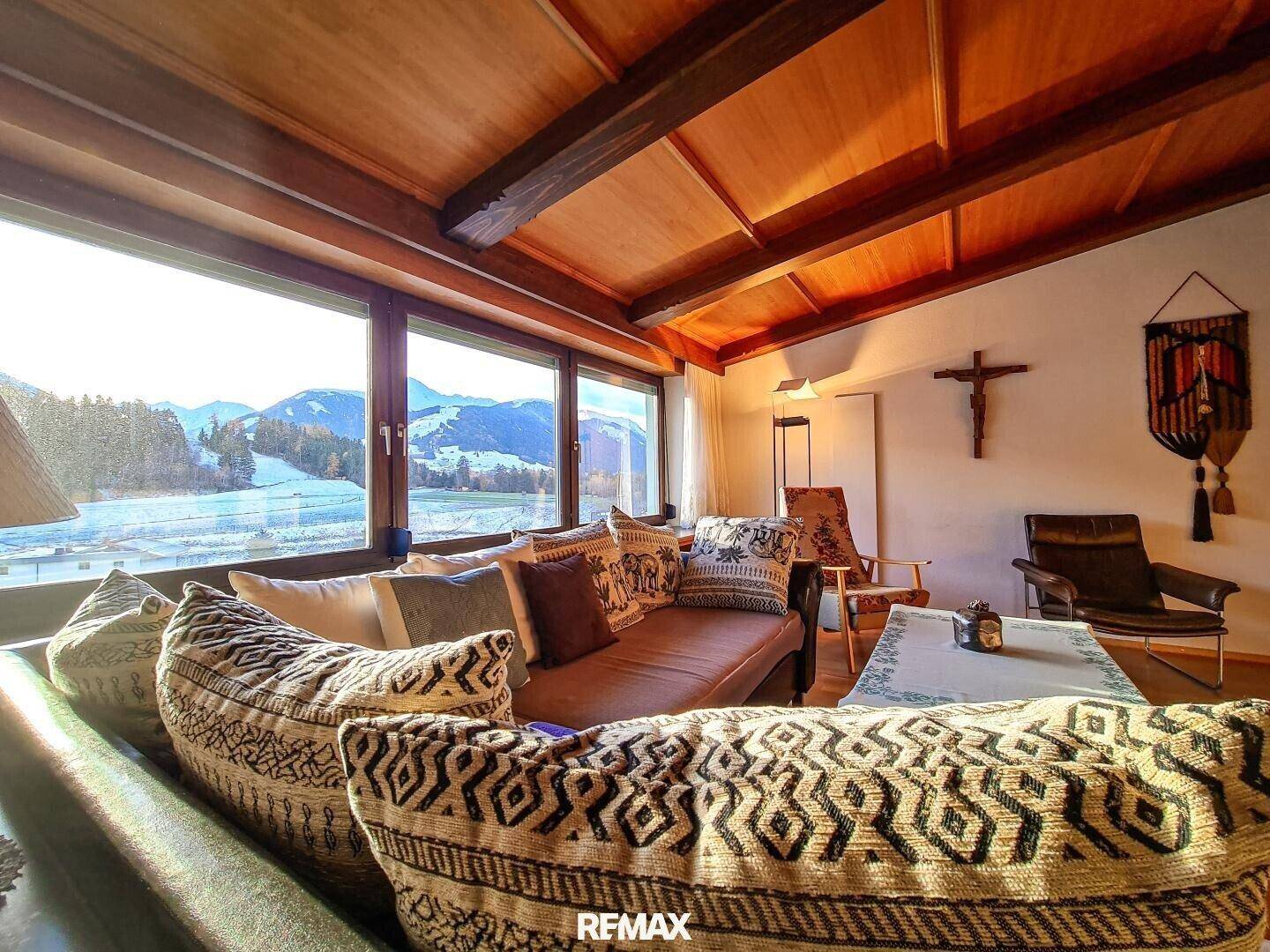 Gemütliches Wohnzimmer im alpinen Stil mit Holzbalkendecke und großzügigem Bergblick durch die Fenster.