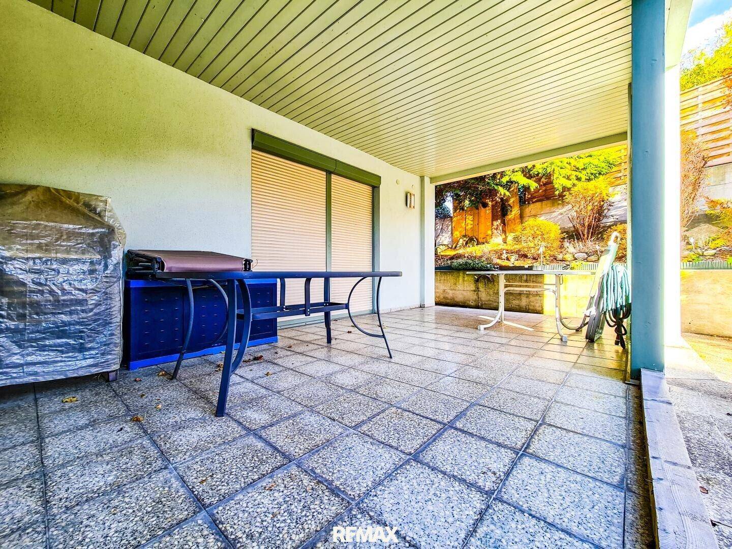 Überdachte Terrasse mit Fliesenboden und Gartenmöbeln, ideal für entspannte Stunden im Freien.