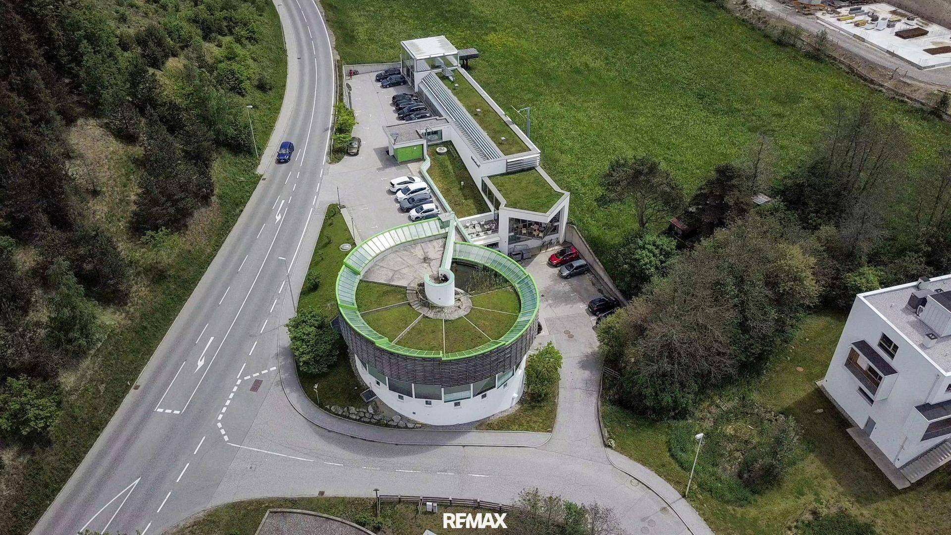 Luftaufnahme des Gebäudekomplexes mit begrünten Dächern, Parkplätzen und umliegenden Straßen im Sommer.