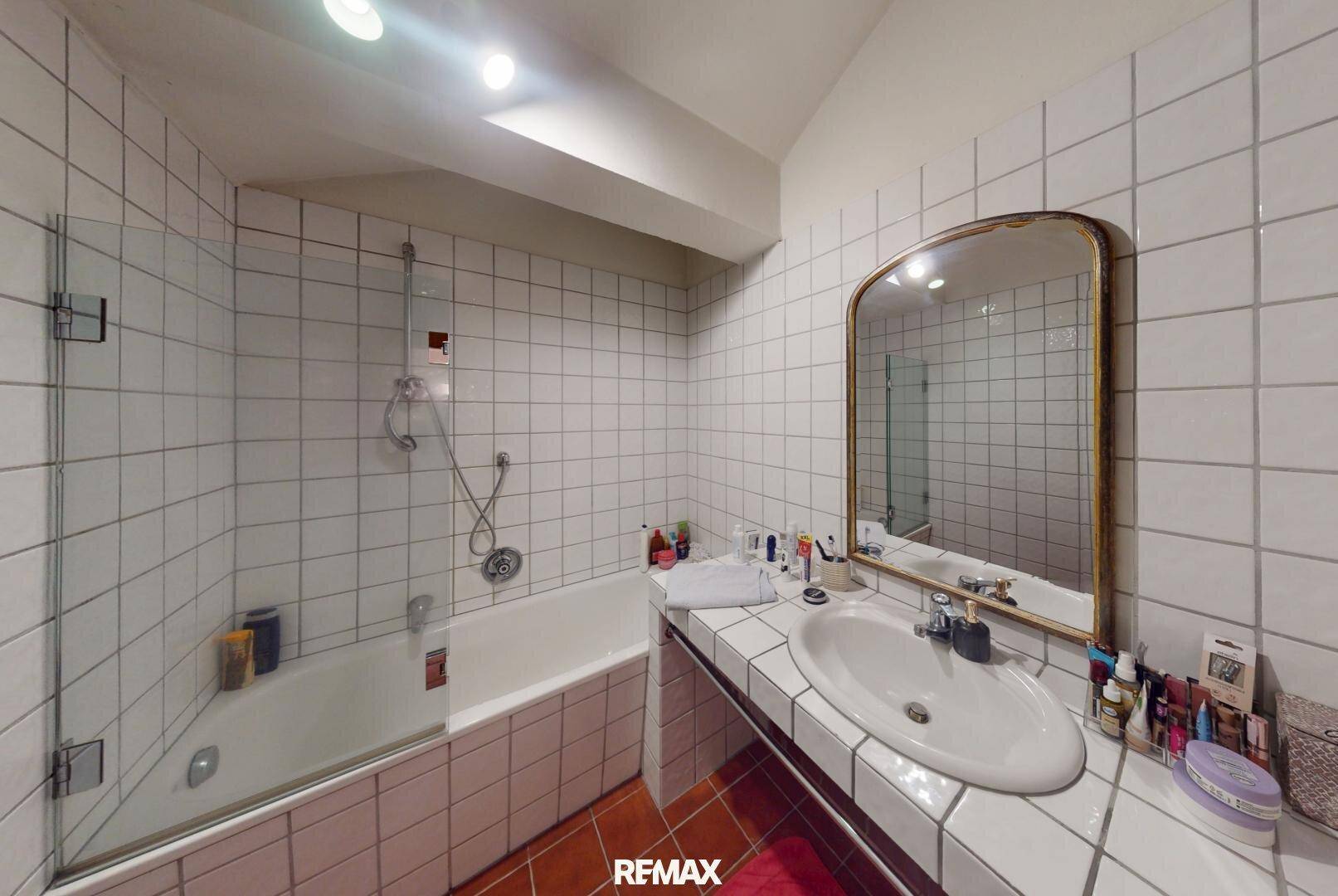 Badezimmer mit Badewanne, Duschbereich und weißen Fliesen an Wänden und Boden.