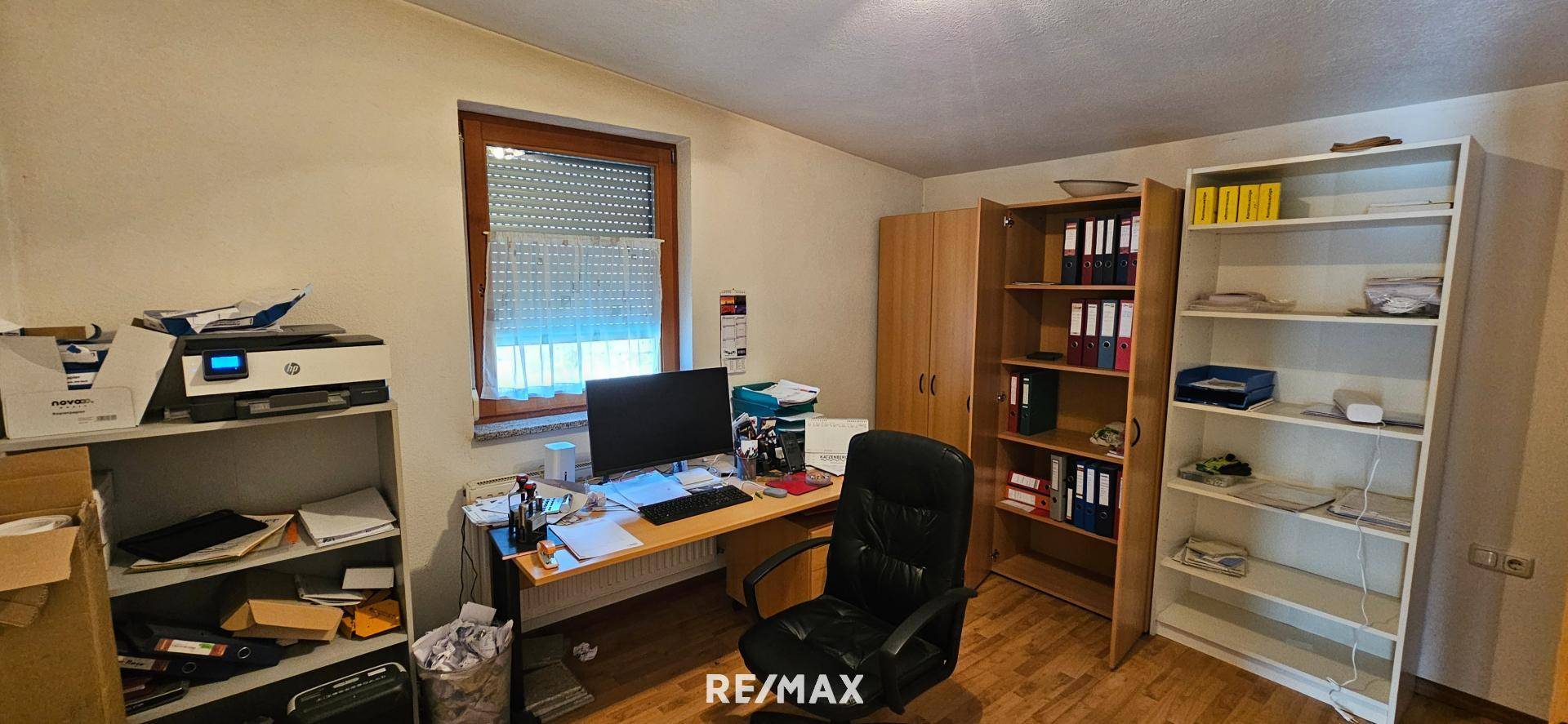 Funktionales Büro mit Schreibtisch, Computer, Bürostuhl und mehreren Regalen für Akten und Bücher.