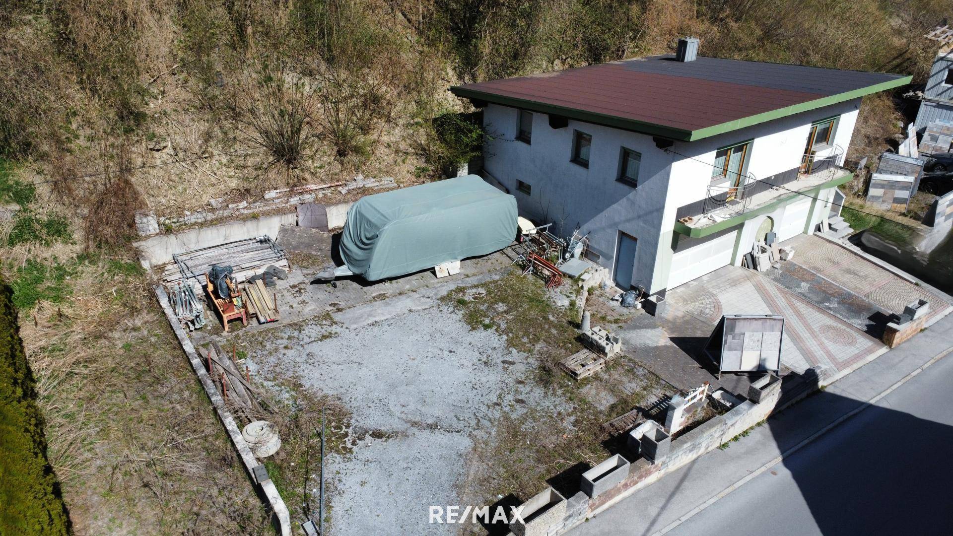 Luftaufnahme des Einfamilienhauses mit großem Grundstück, Kiesfläche und angrenzendem Hang, umgeben von Natur.
