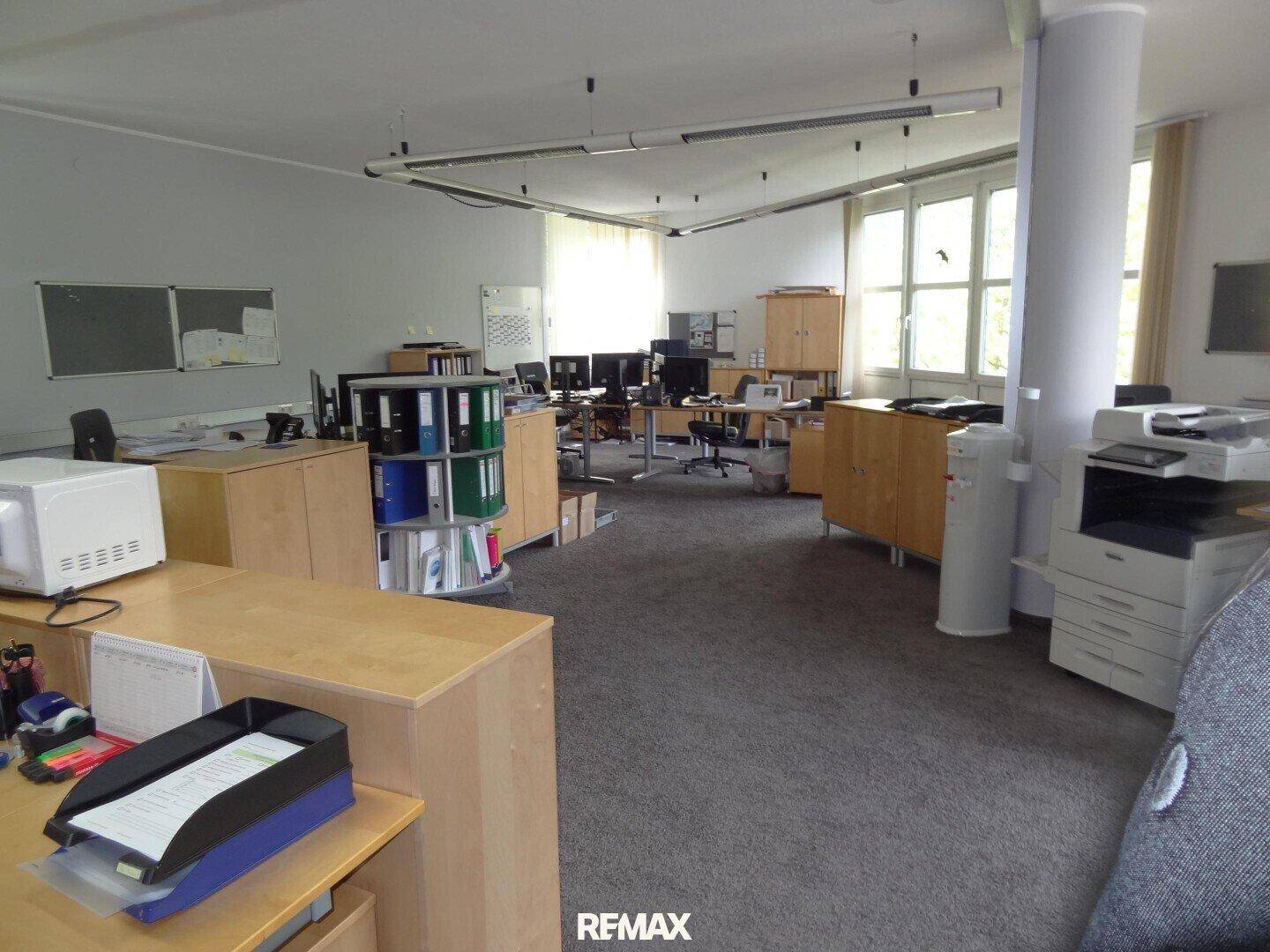 Großes, offenes Büro mit mehreren Arbeitsplätzen, Teppichboden und Aktenschränken.