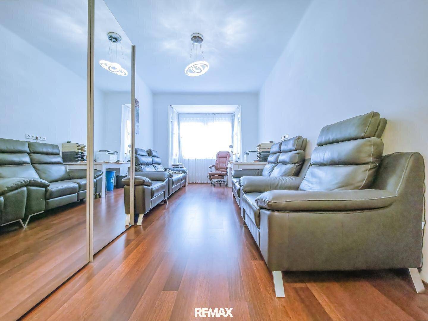 Geräumiges Wohnzimmer mit Ledersofas, Holzboden und großem Fenster.
